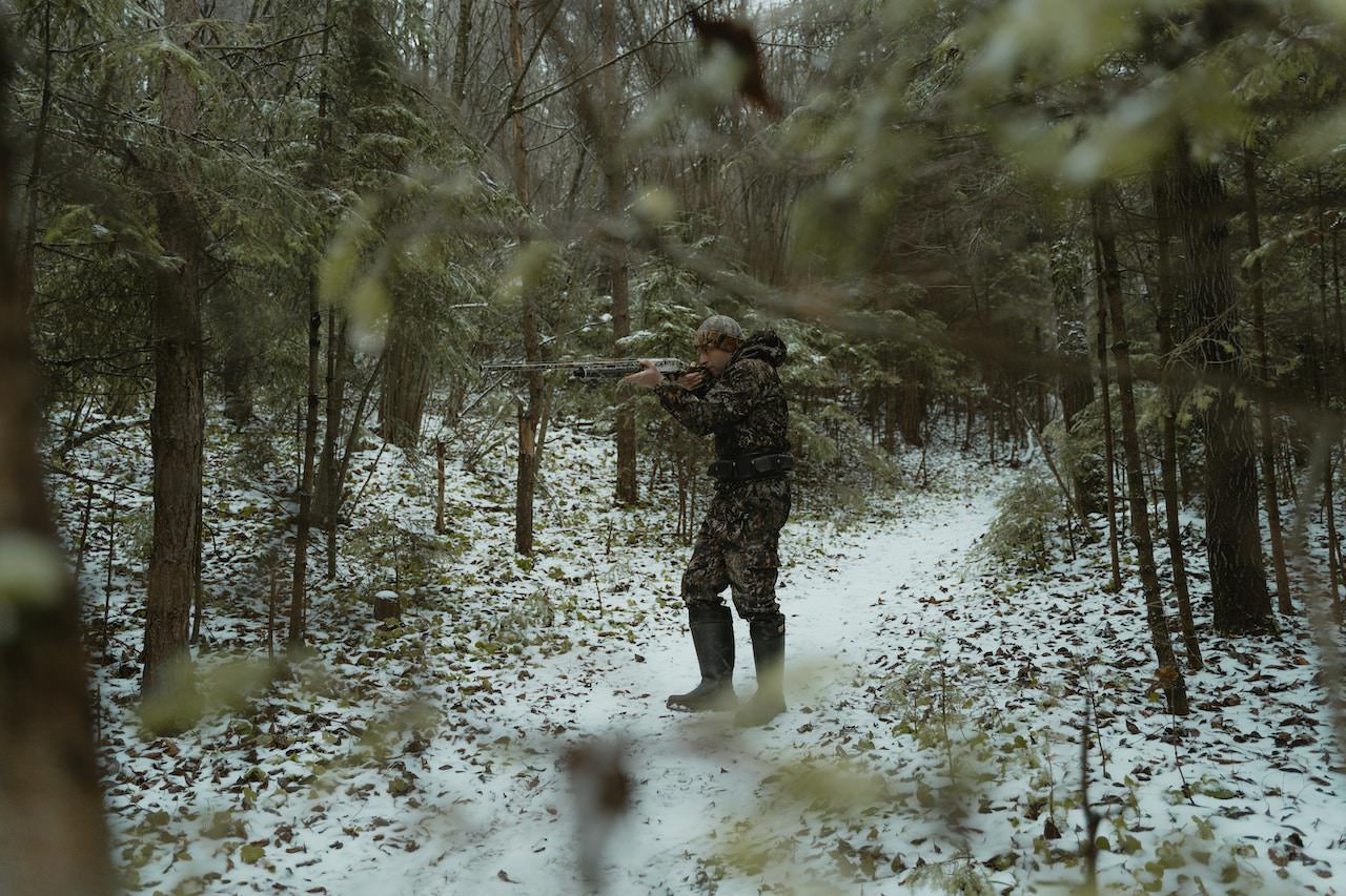 Male hunter in camouflage point a rifle in the woods.